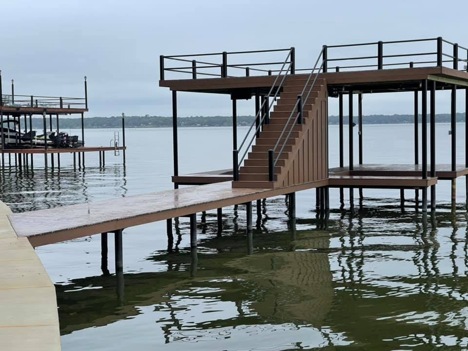 A brown dock on the water pictured with stairs and darker accents